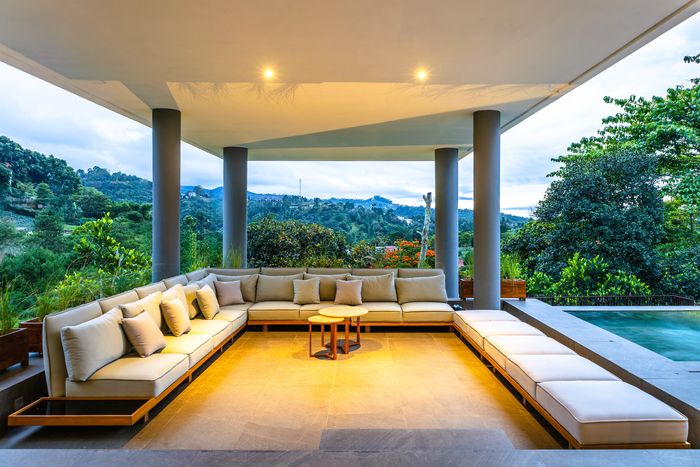 Lounge semi terbuka dengan sofa besar menghadap kolam renang dan perbukitan
